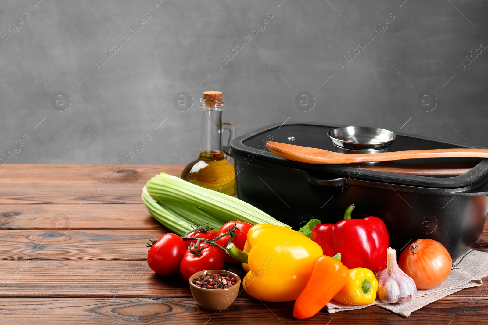 Photo of Black pot with glass lid, different products and spoon on wooden table