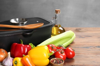 Photo of Black pot with glass lid, different products and spoon on wooden table