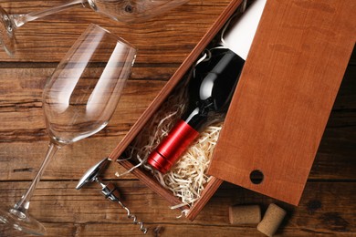 Photo of Box with wine bottle, glasses, corkscrew and corks on wooden table, flat lay