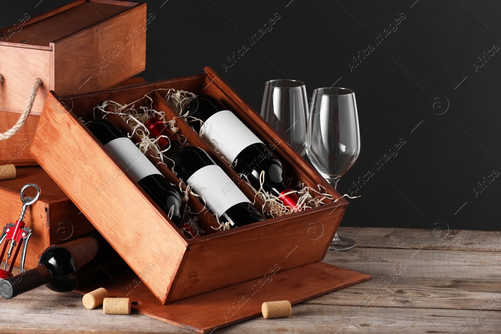 Photo of Box with wine bottles and glasses on wooden table against black background. Space for text