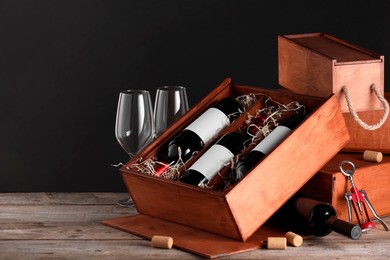 Box with wine bottles and glasses on wooden table against black background. Space for text