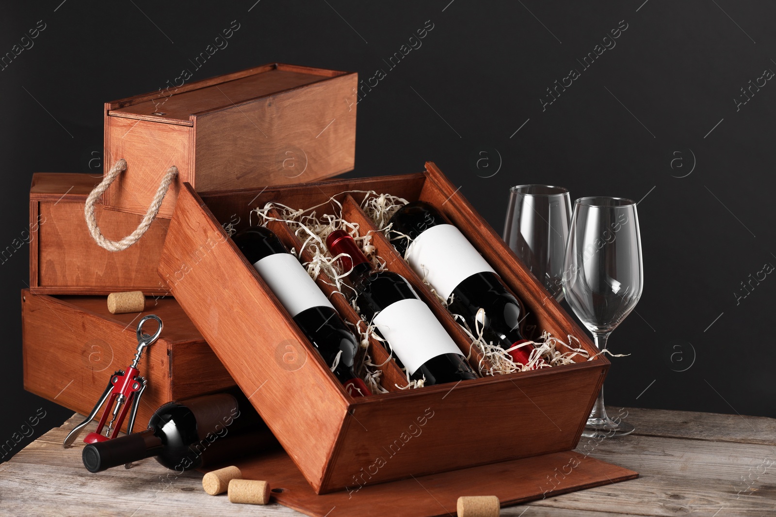 Photo of Box with wine bottles and glasses on wooden table against black background