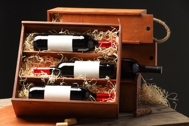 Photo of Box with wine bottles on wooden table against black background