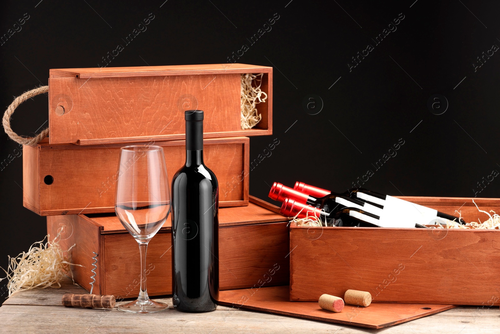 Photo of Boxes with wine bottles, corks and glass on wooden table against black background