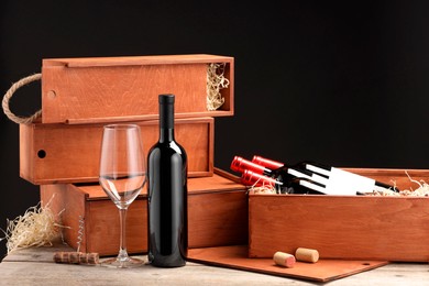 Photo of Boxes with wine bottles, corks and glass on wooden table against black background