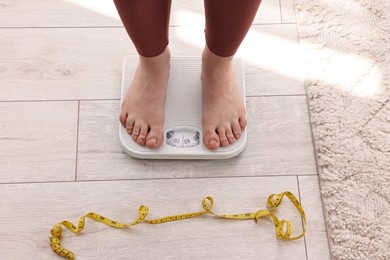 Photo of Woman standing on floor scale and measuring tape at home, top view. Weight control