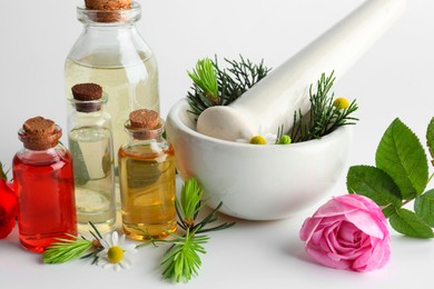 Photo of Aromatherapy. Different essential oils, flowers, mortar, pestle and fir twigs on white background