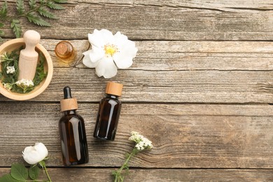 Photo of Aromatherapy. Different essential oils, flowers, green leaves, mortar and pestle on wooden table, flat lay. Space for text