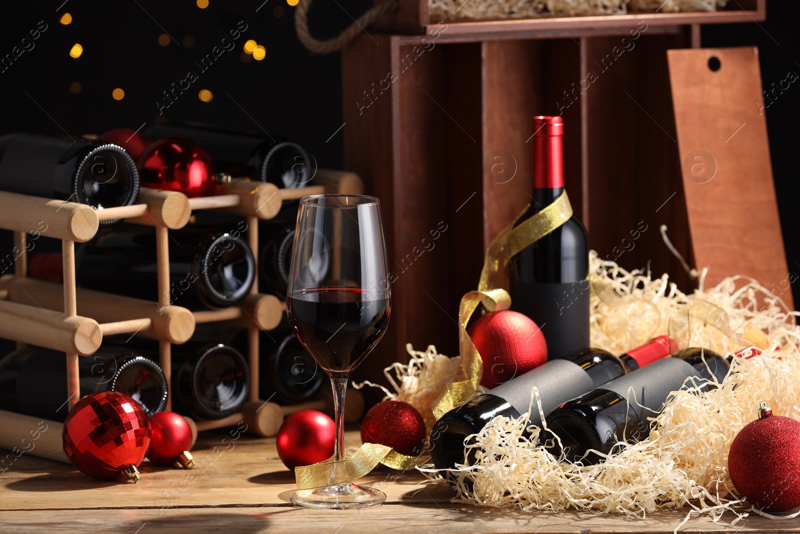 Photo of Bottles of wine, glass, wooden box, corks and red Christmas balls on table