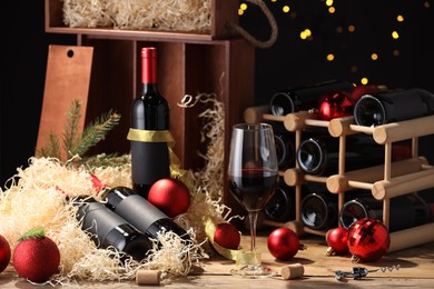 Photo of Bottles of wine, glass, wooden boxes, corks and red Christmas balls on table