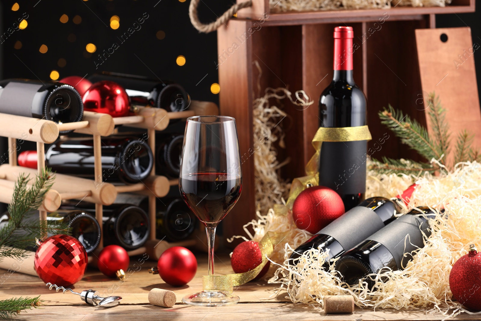 Photo of Bottles of wine, glass, wooden box, corks and red Christmas balls on table