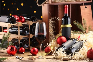 Photo of Bottles of wine, glass, wooden box, corks and red Christmas balls on table