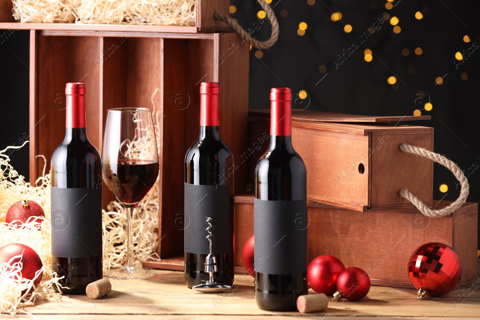 Photo of Bottles of wine, glass, wooden boxes, corks and red Christmas balls on table