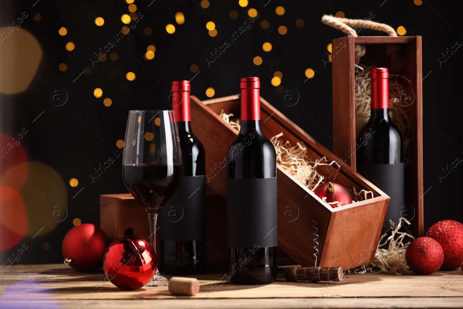 Photo of Bottles of wine, glass, wooden boxes, corkscrew and red Christmas balls on table