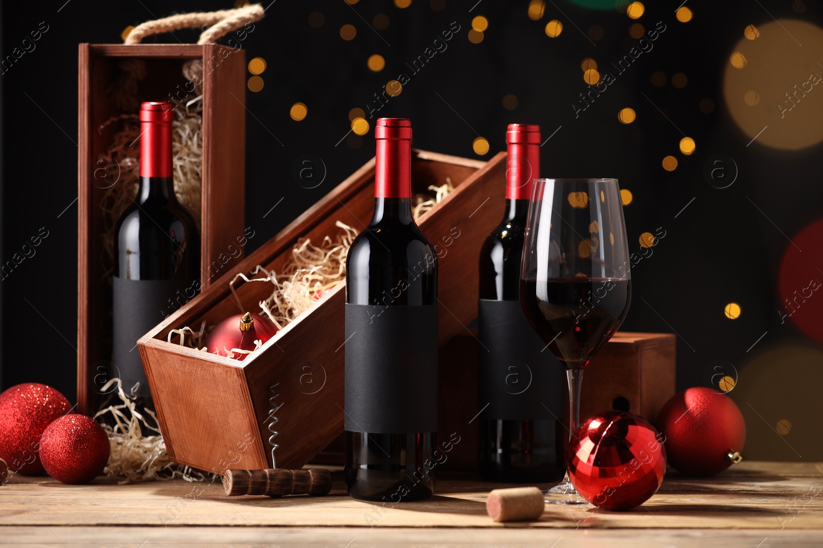 Photo of Bottles of wine, glass, wooden boxes, corkscrew and red Christmas balls on table