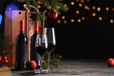 Photo of Bottles of wine, glasses, wooden boxes, fir twigs and red Christmas balls on table, space for text