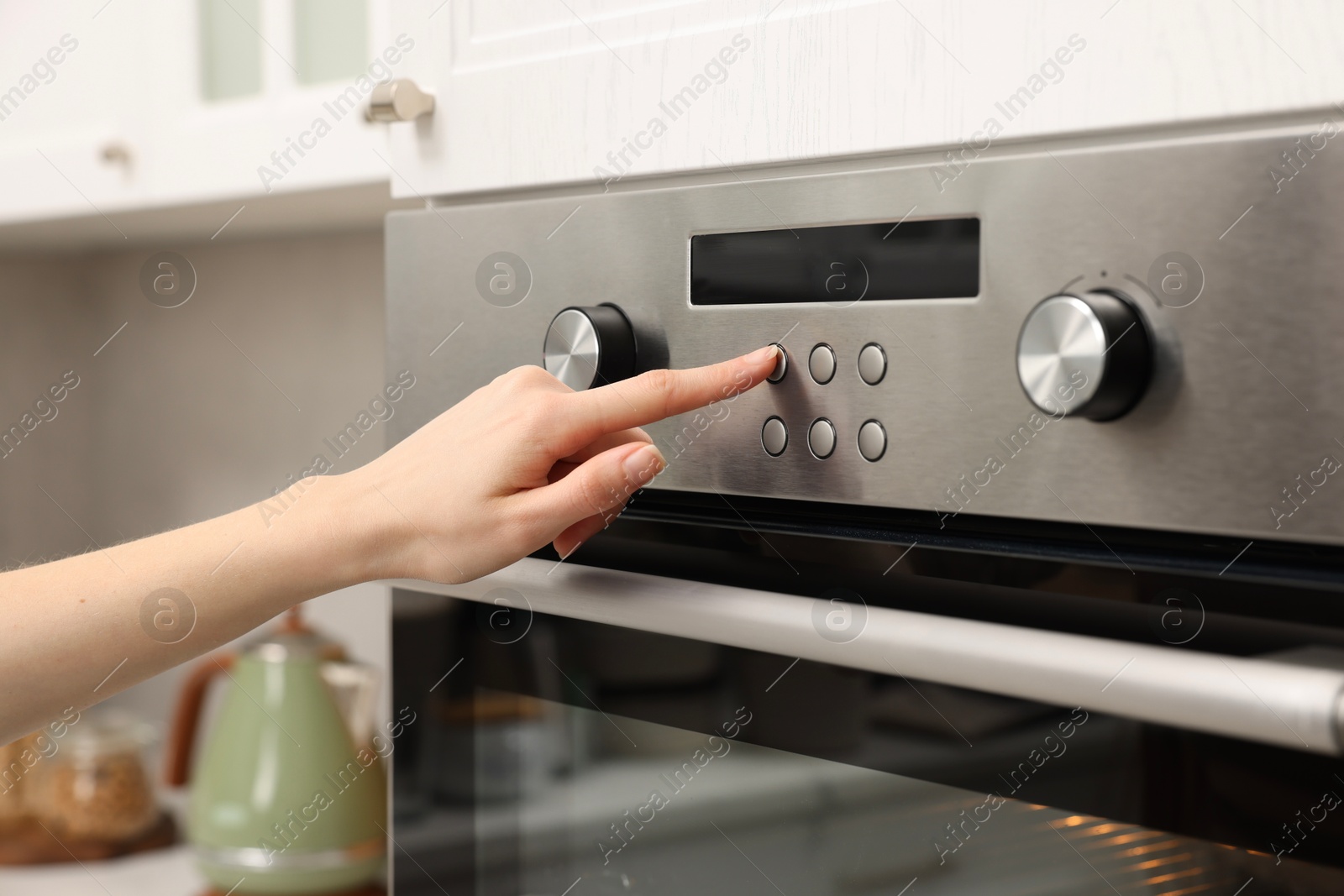 Photo of Woman using electric oven in kitchen, closeup