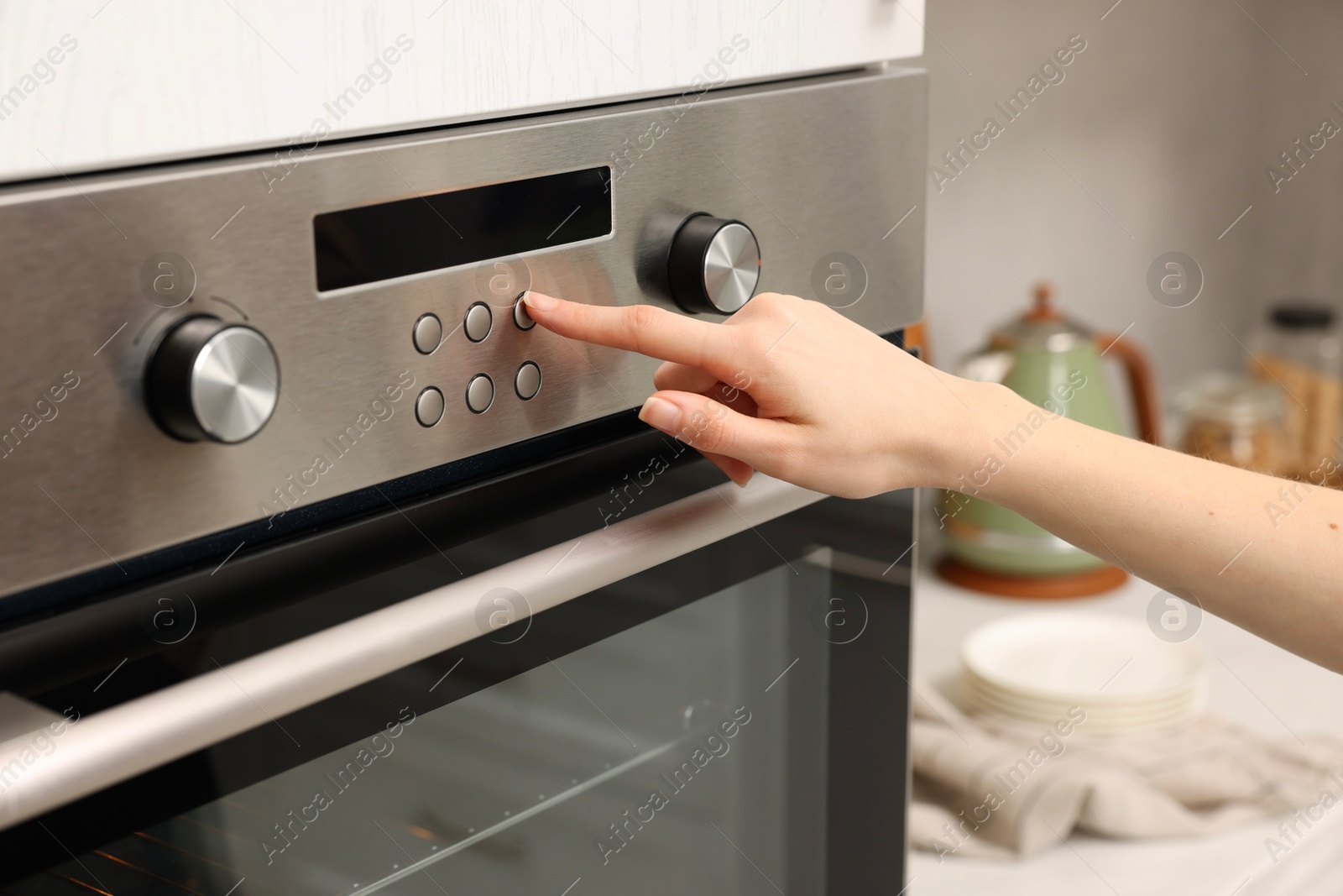 Photo of Woman using electric oven in kitchen, closeup