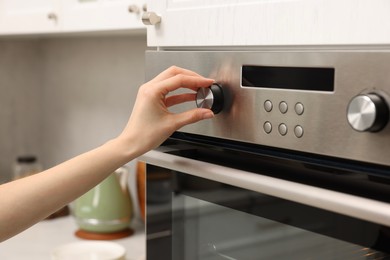 Woman using electric oven in kitchen, closeup