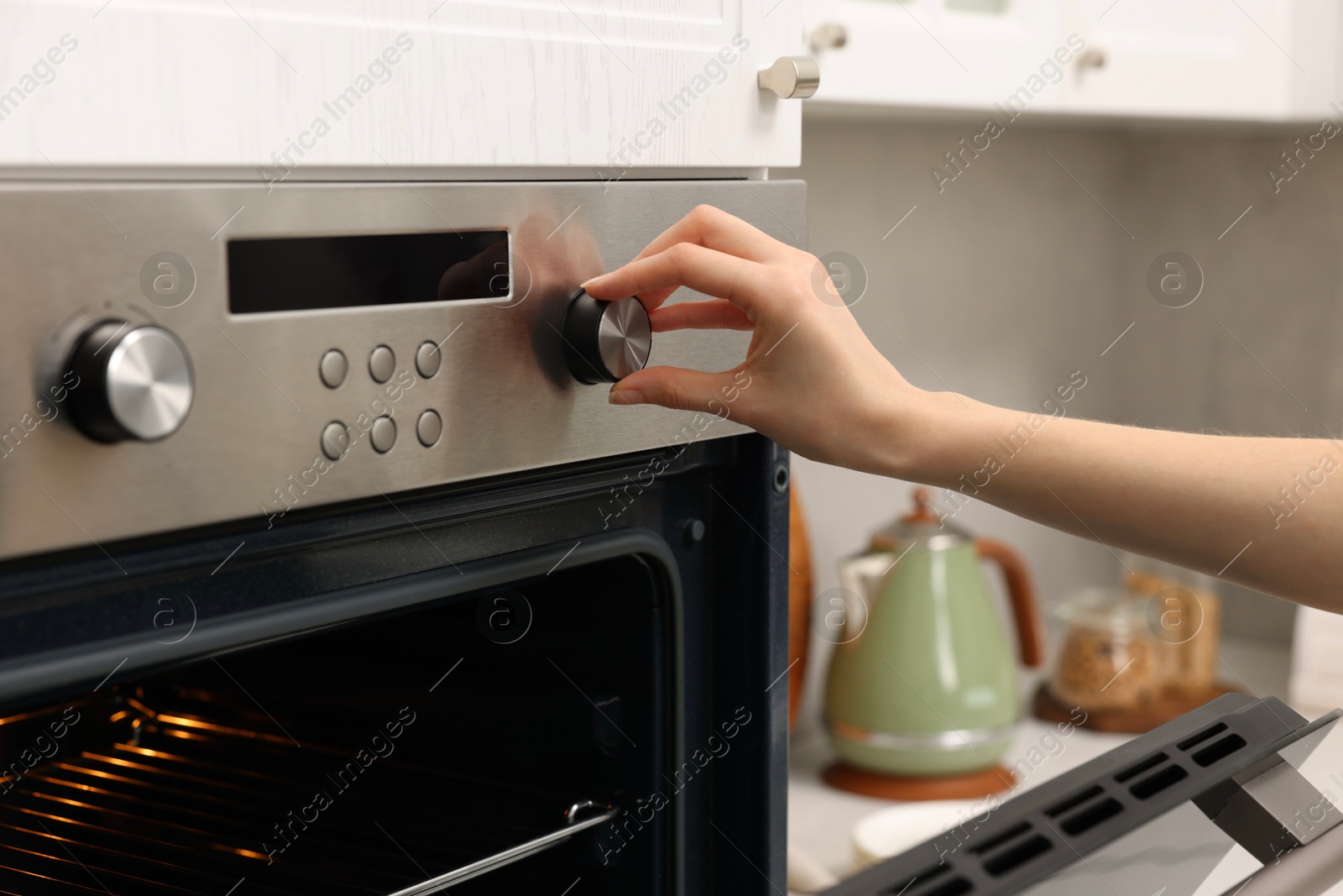 Photo of Woman using electric oven in kitchen, closeup