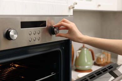 Photo of Woman using electric oven in kitchen, closeup