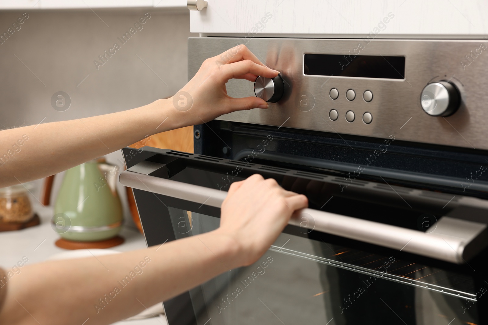 Photo of Woman using electric oven in kitchen, closeup