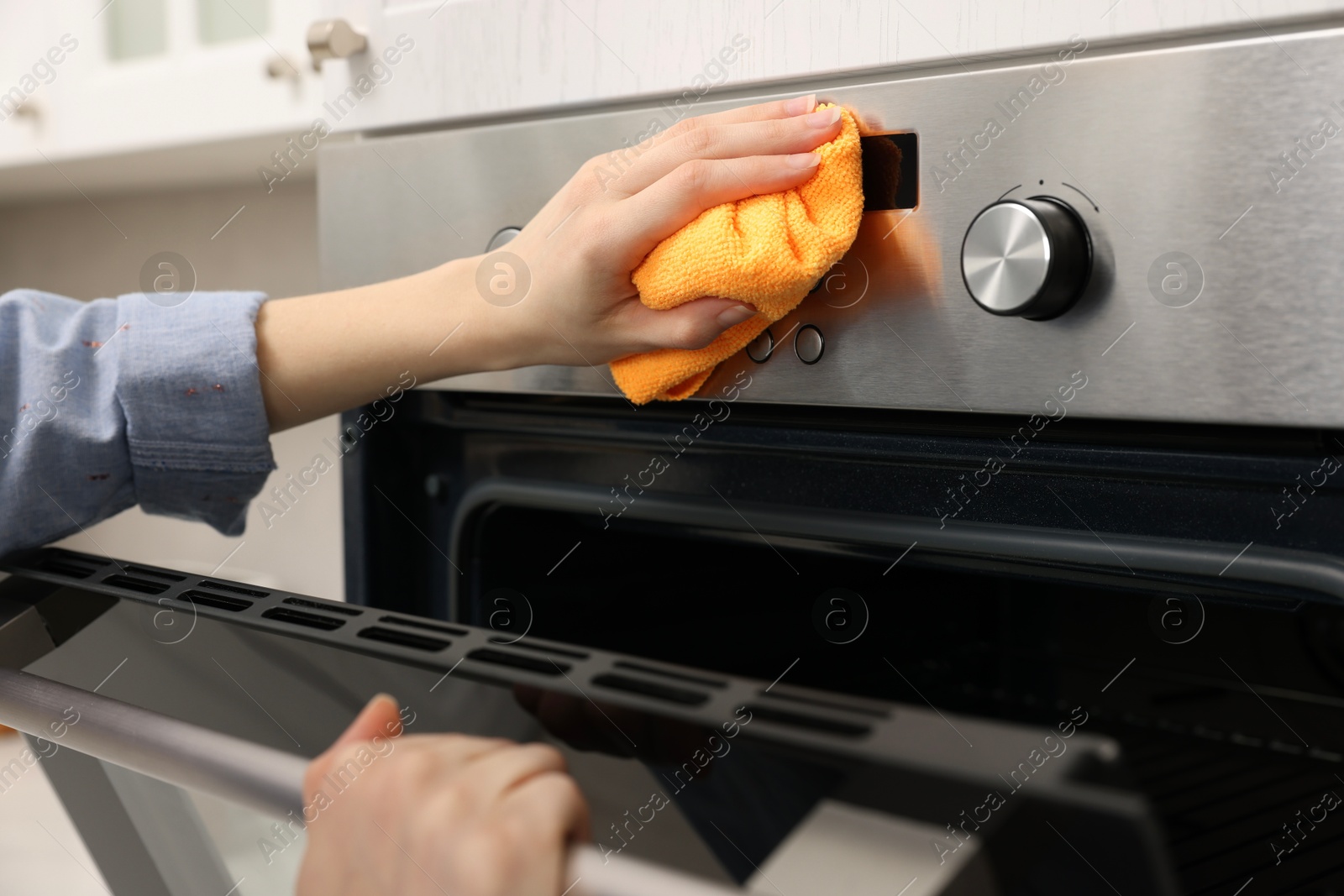 Photo of Woman cleaning electric oven with rag in kitchen, closeup