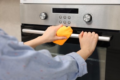 Photo of Woman cleaning electric oven with rag in kitchen, closeup