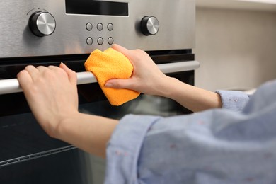 Photo of Woman cleaning electric oven with rag in kitchen, closeup