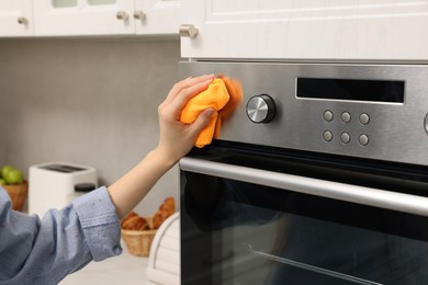 Photo of Woman cleaning electric oven with rag in kitchen, closeup