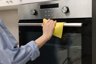 Woman cleaning electric oven with rag in kitchen, closeup