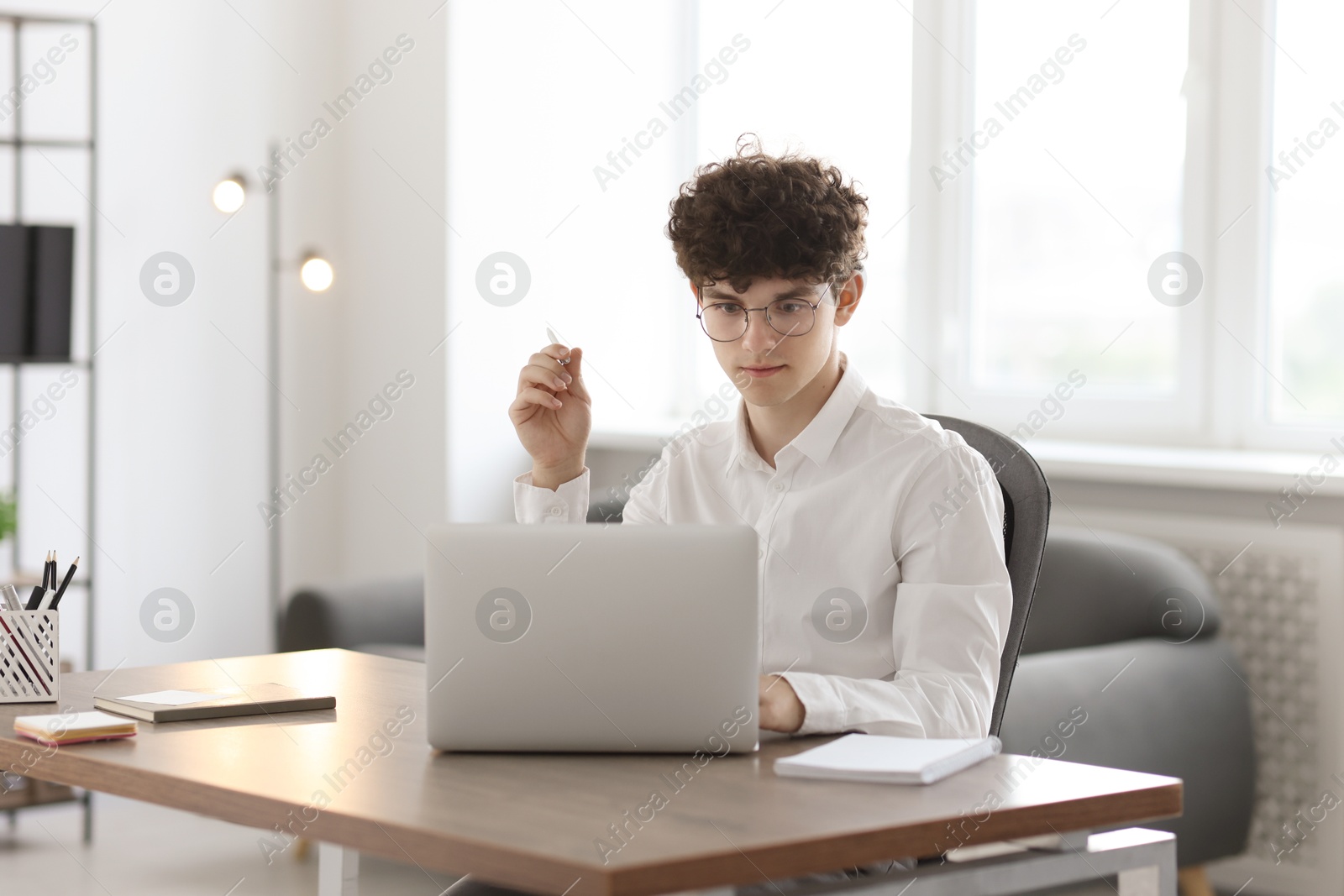 Photo of Teenager with pen working on laptop at table indoors. Remote job