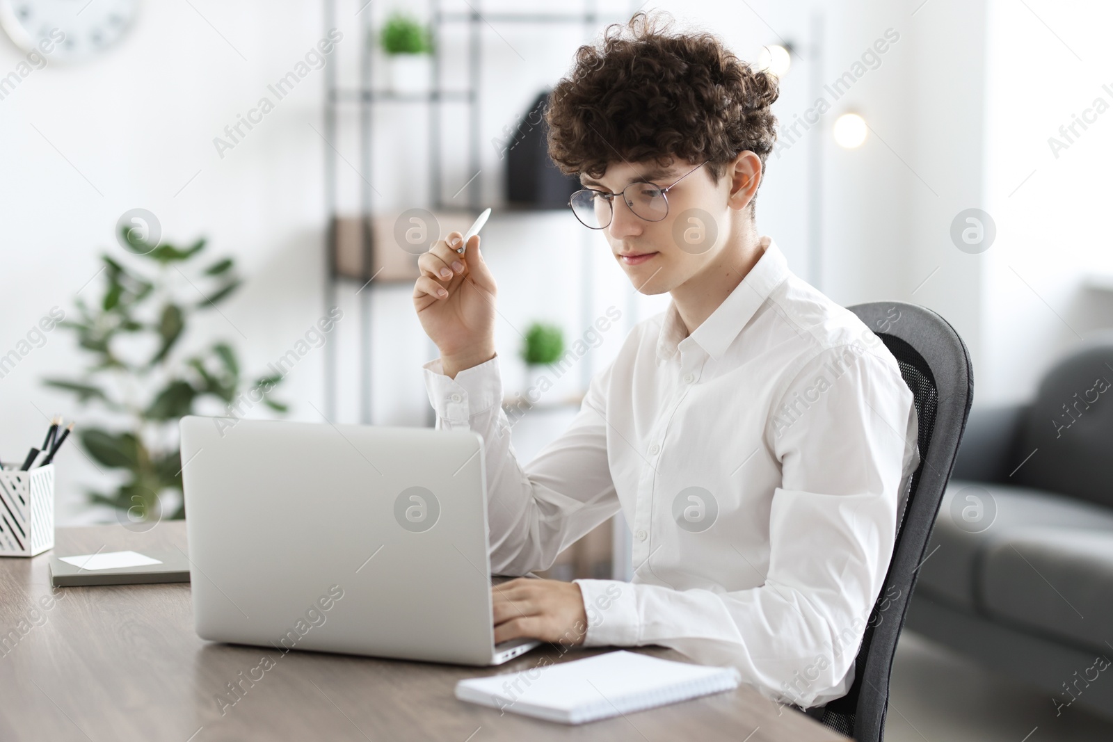 Photo of Teenager with pen working on laptop at table indoors. Remote job