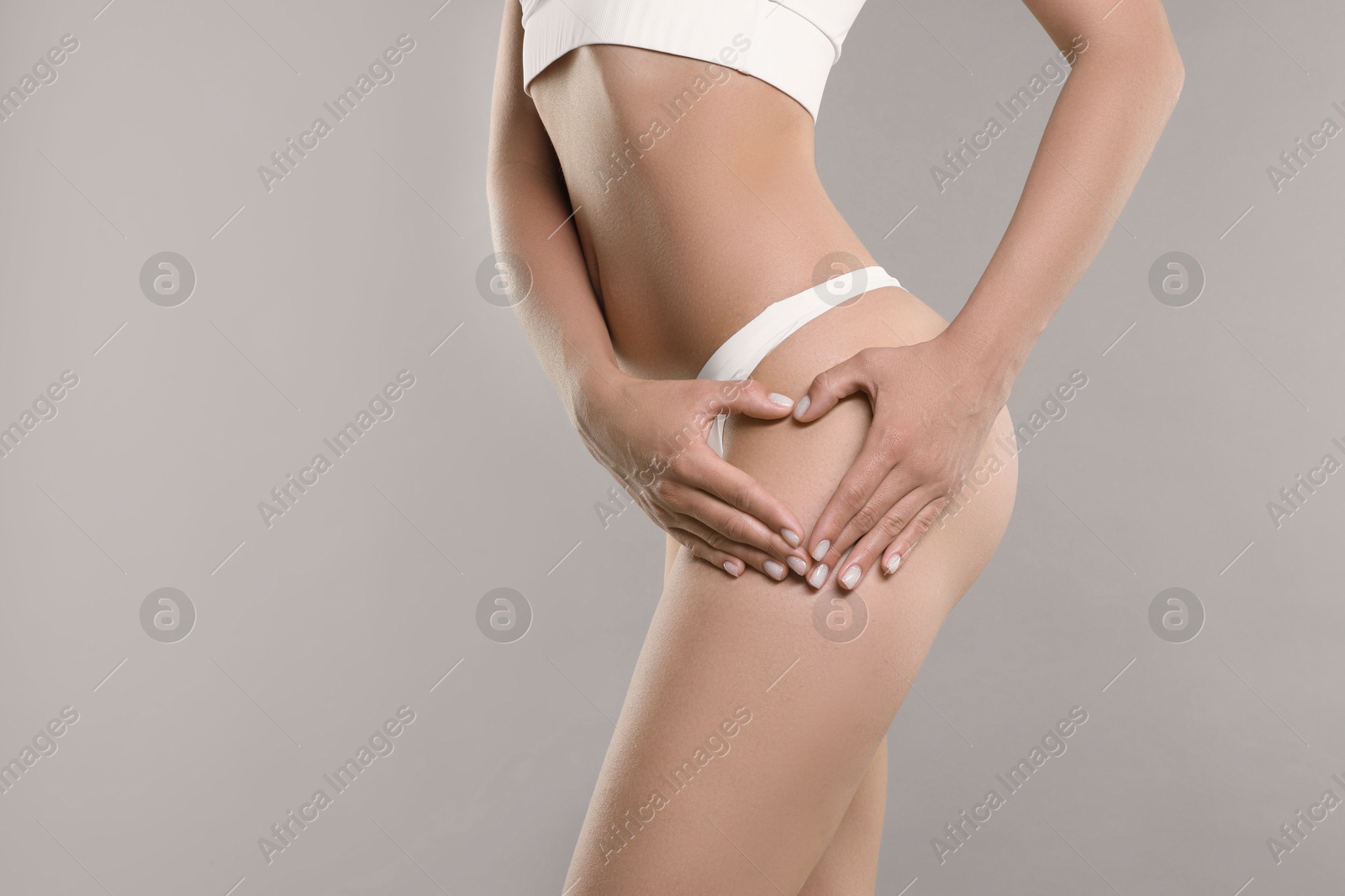 Photo of Woman in underwear making heart with hands near thigh on light grey background, closeup. Cellulite problem