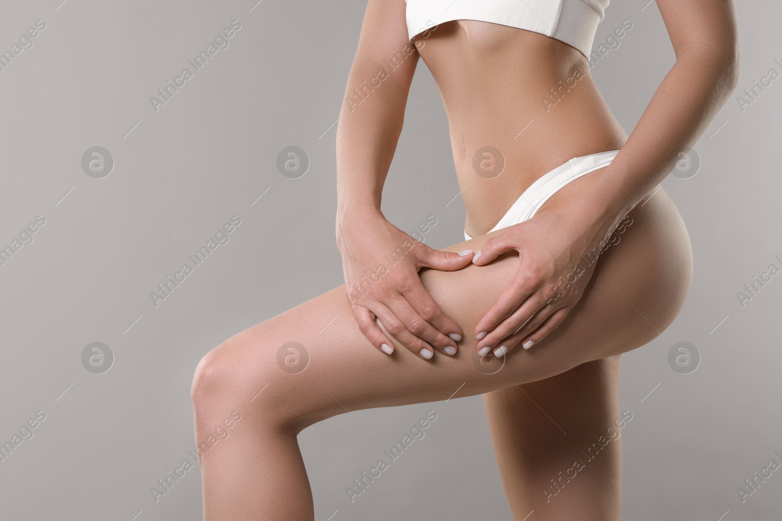 Photo of Woman in underwear making heart with hands near thigh on light grey background, closeup. Cellulite problem