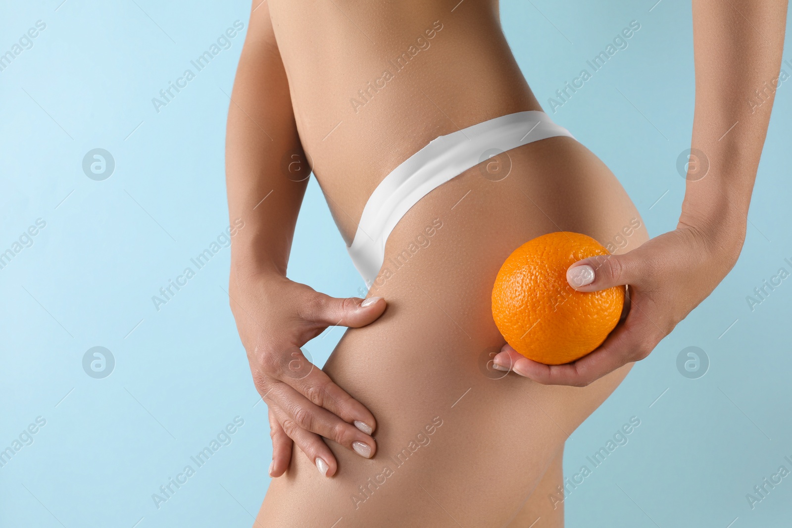 Photo of Woman in underwear with orange on light blue background, closeup. Cellulite problem