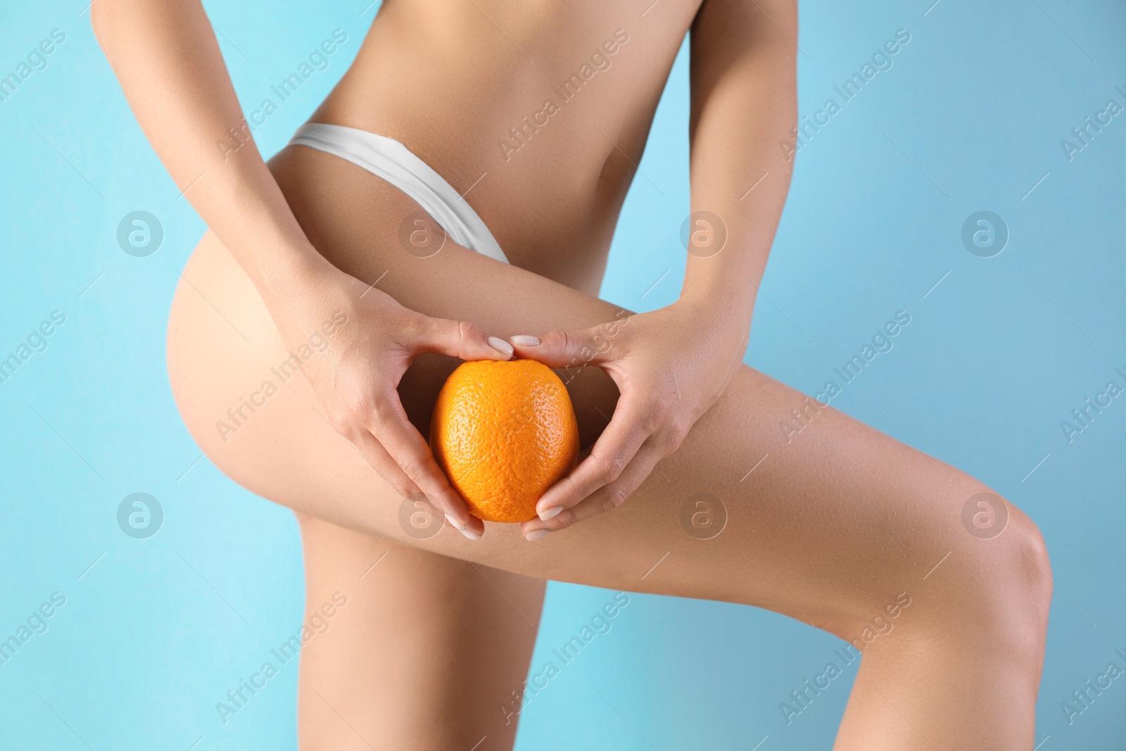 Photo of Woman in underwear with orange on light blue background, closeup. Cellulite problem