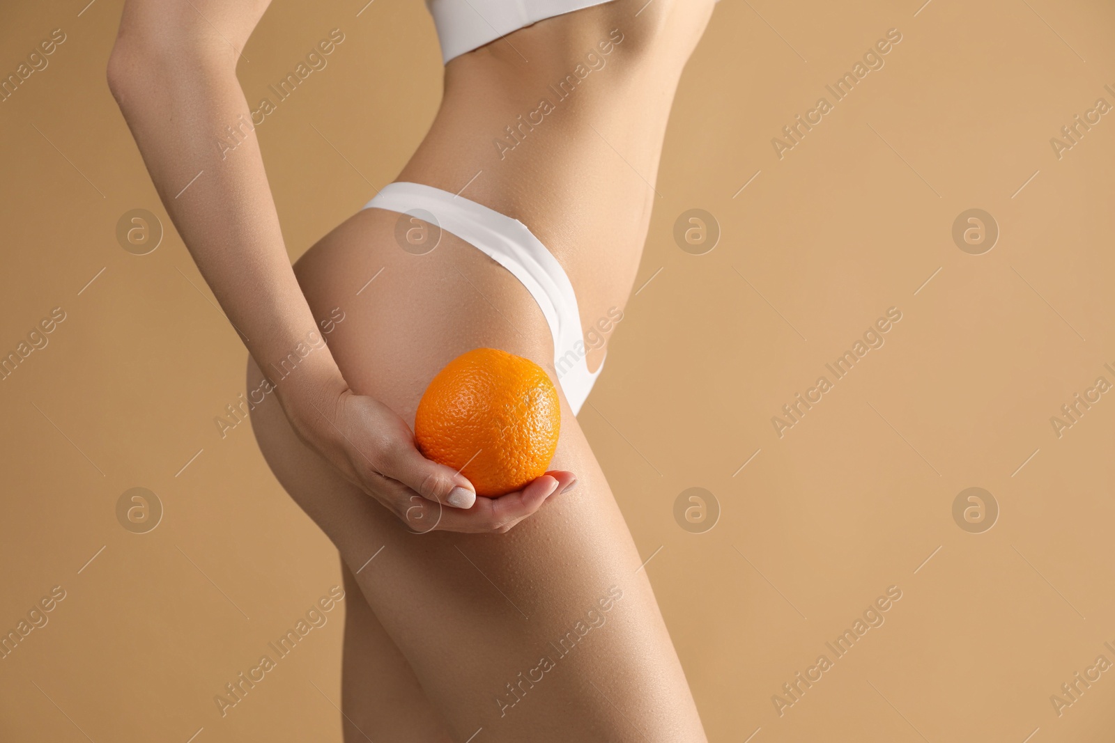 Photo of Woman in underwear with orange on beige background, closeup. Cellulite problem