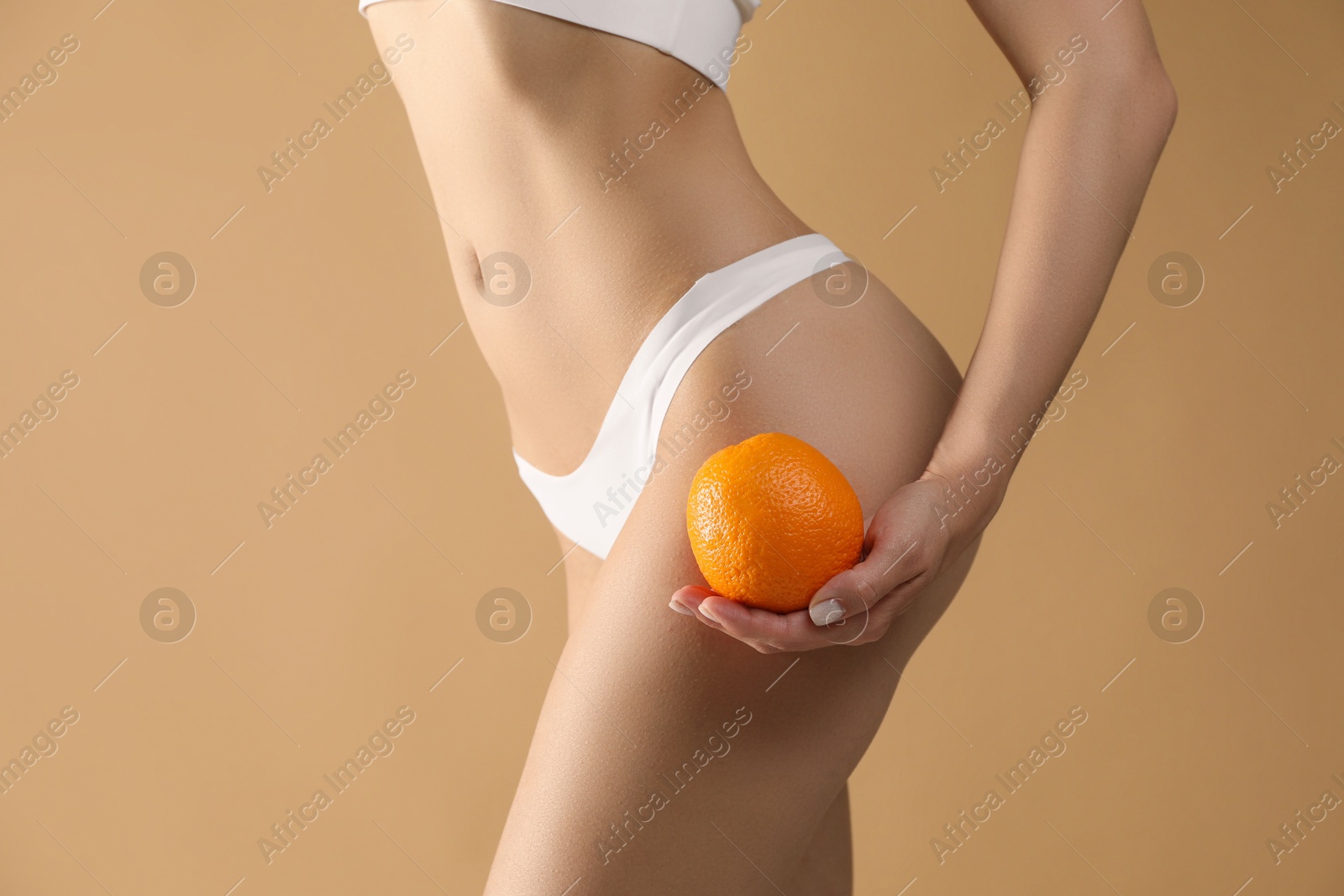 Photo of Woman in underwear with orange on beige background, closeup. Cellulite problem