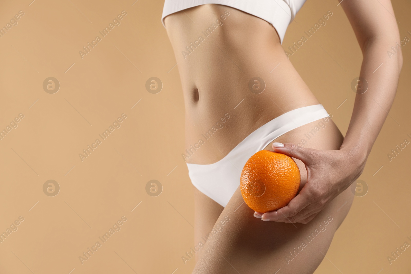 Photo of Woman in underwear with orange on beige background, closeup. Cellulite problem