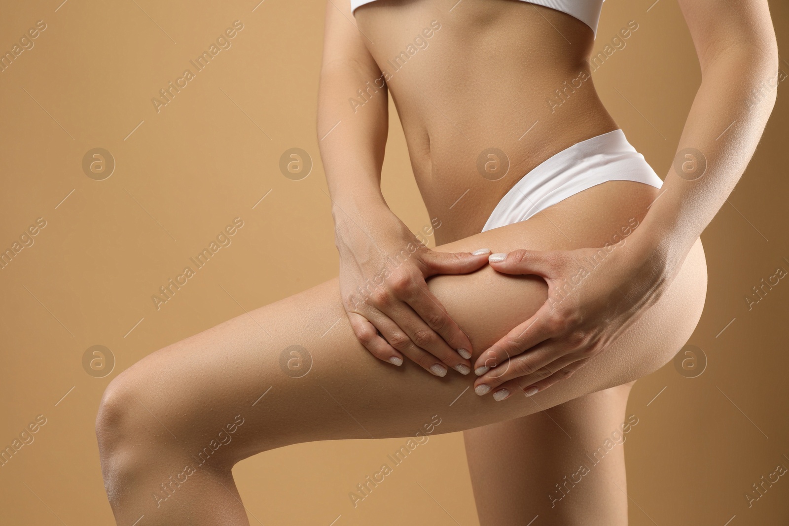 Photo of Woman in underwear making heart with hands near thigh on beige background, closeup. Cellulite problem