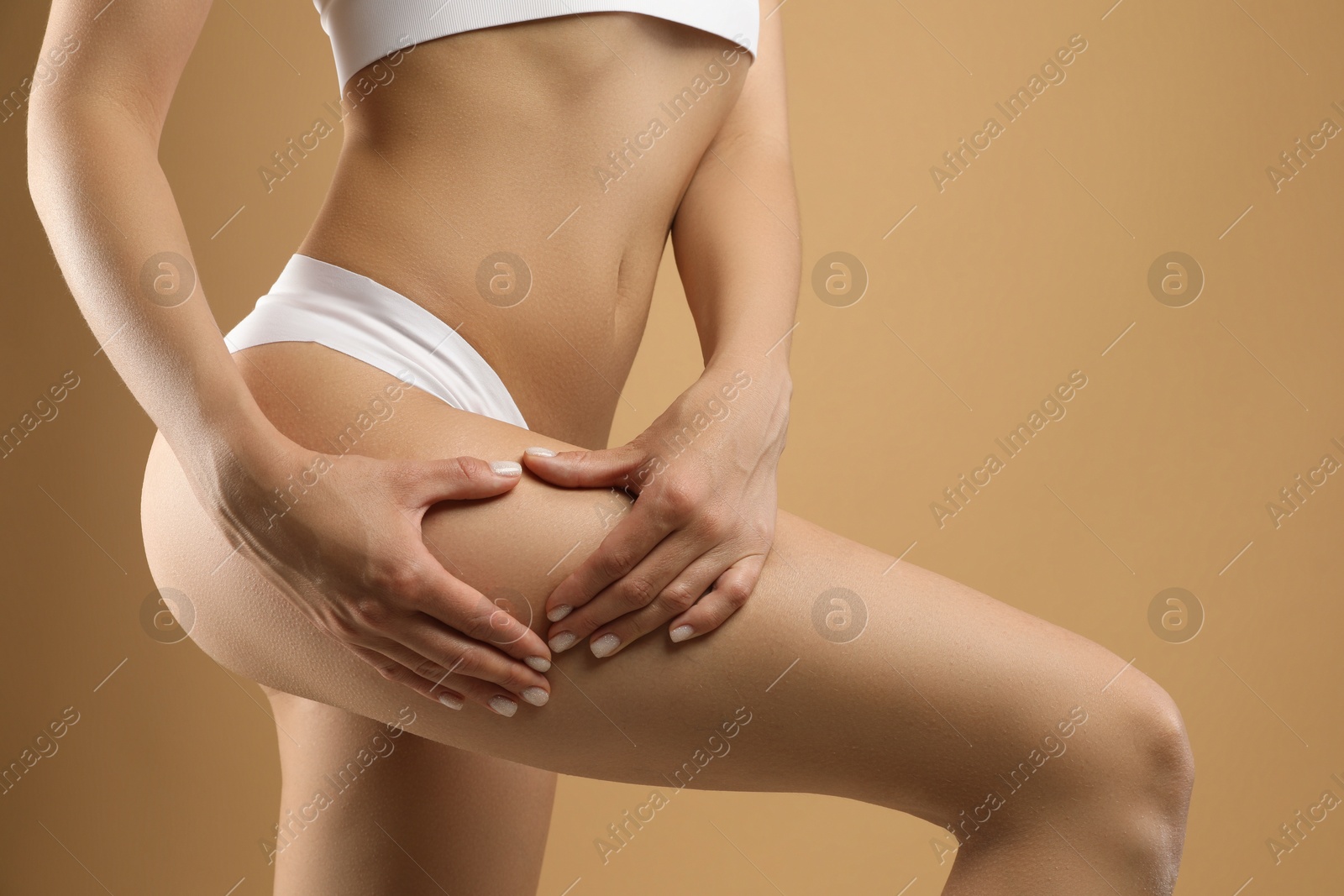 Photo of Woman in underwear making heart with hands near thigh on beige background, closeup. Cellulite problem