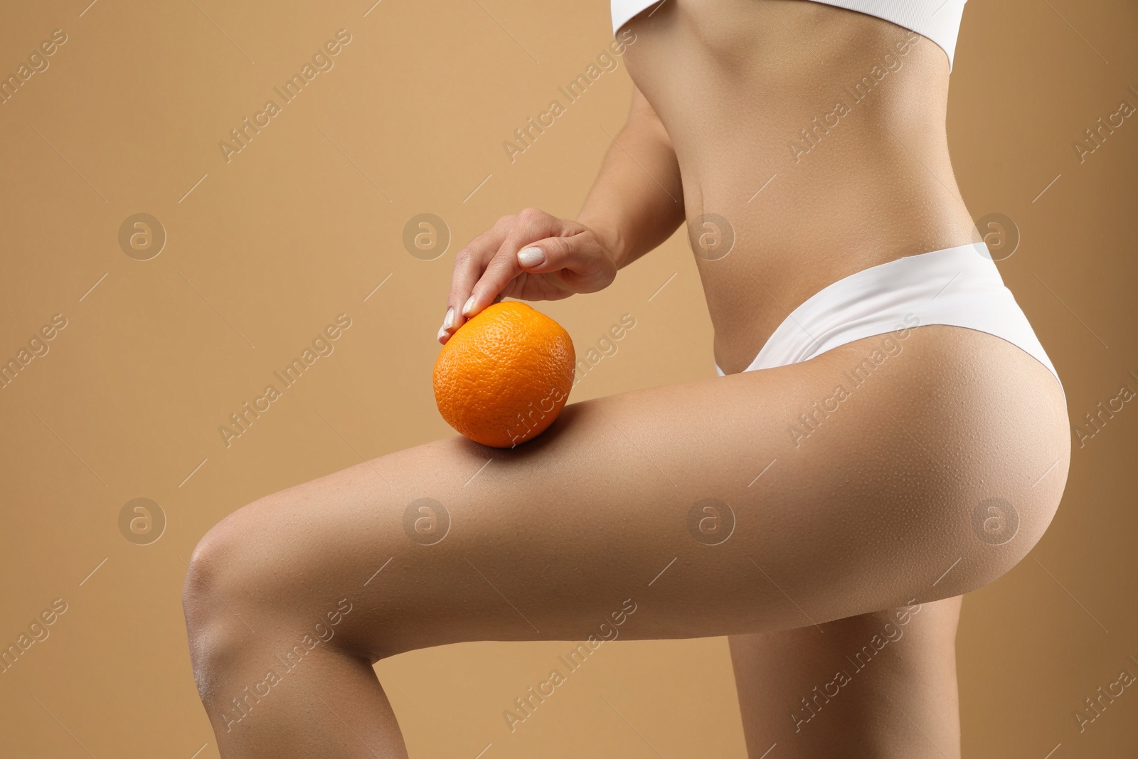 Photo of Woman in underwear with orange on beige background, closeup. Cellulite problem