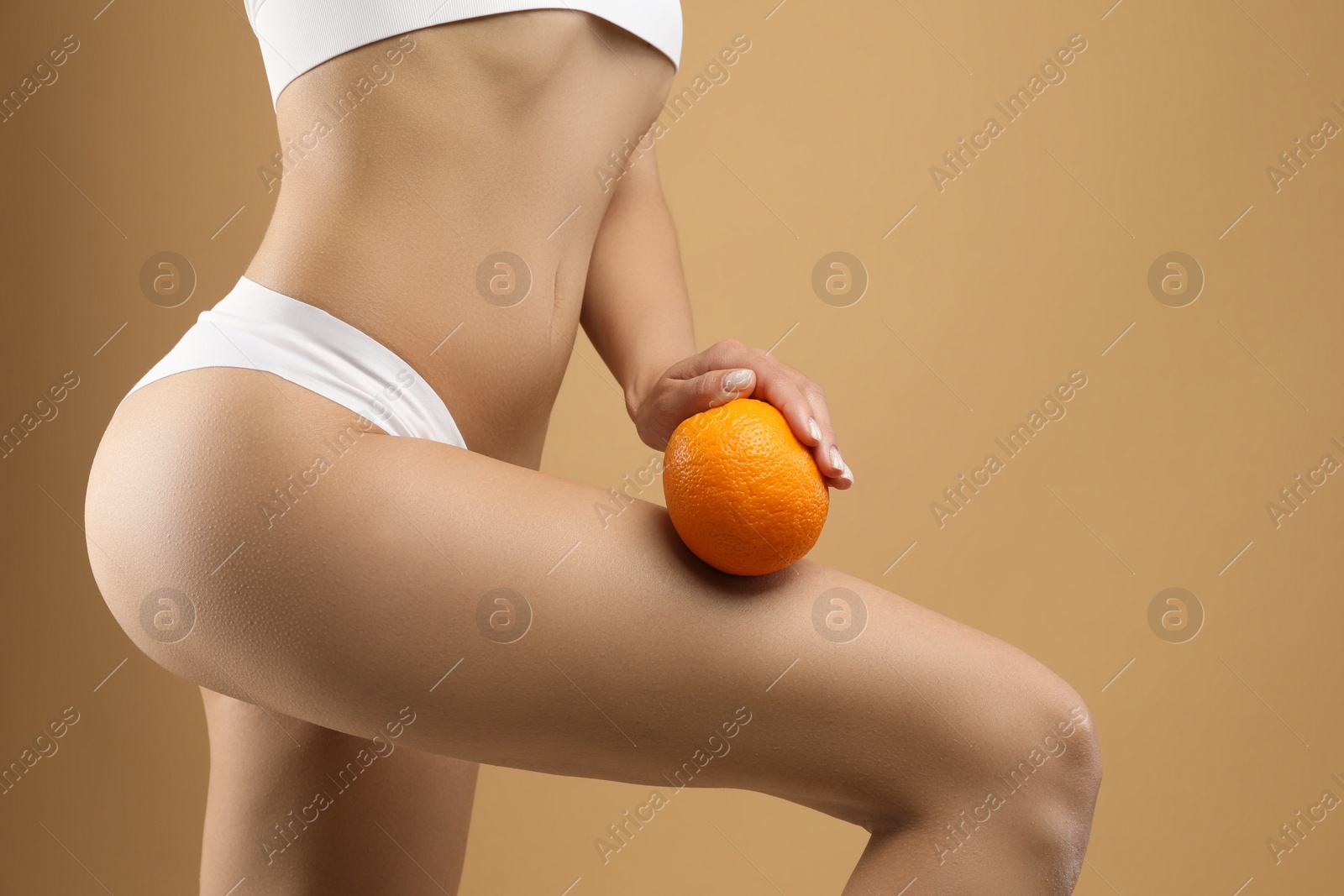 Photo of Woman in underwear with orange on beige background, closeup. Cellulite problem