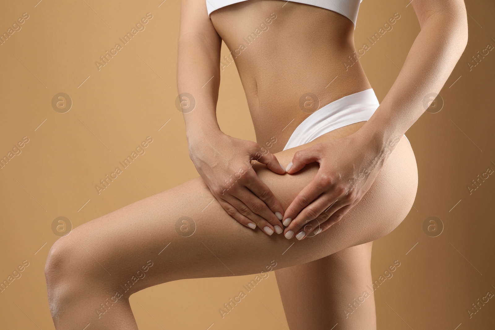 Photo of Woman in underwear making heart with hands near thigh on beige background, closeup. Cellulite problem