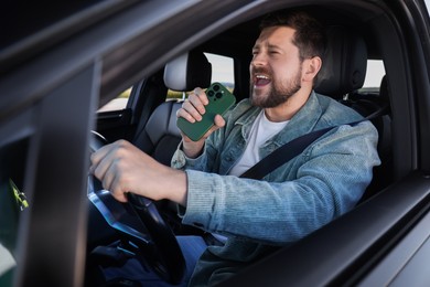 Photo of Man with smartphone singing in car, view from outside