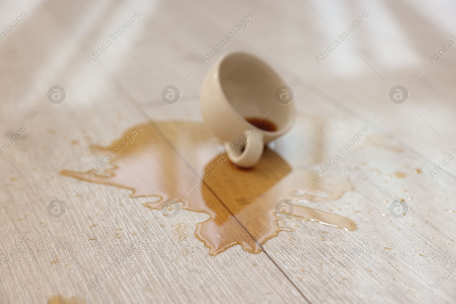 Photo of Cup with spilled drink on wooden floor, closeup