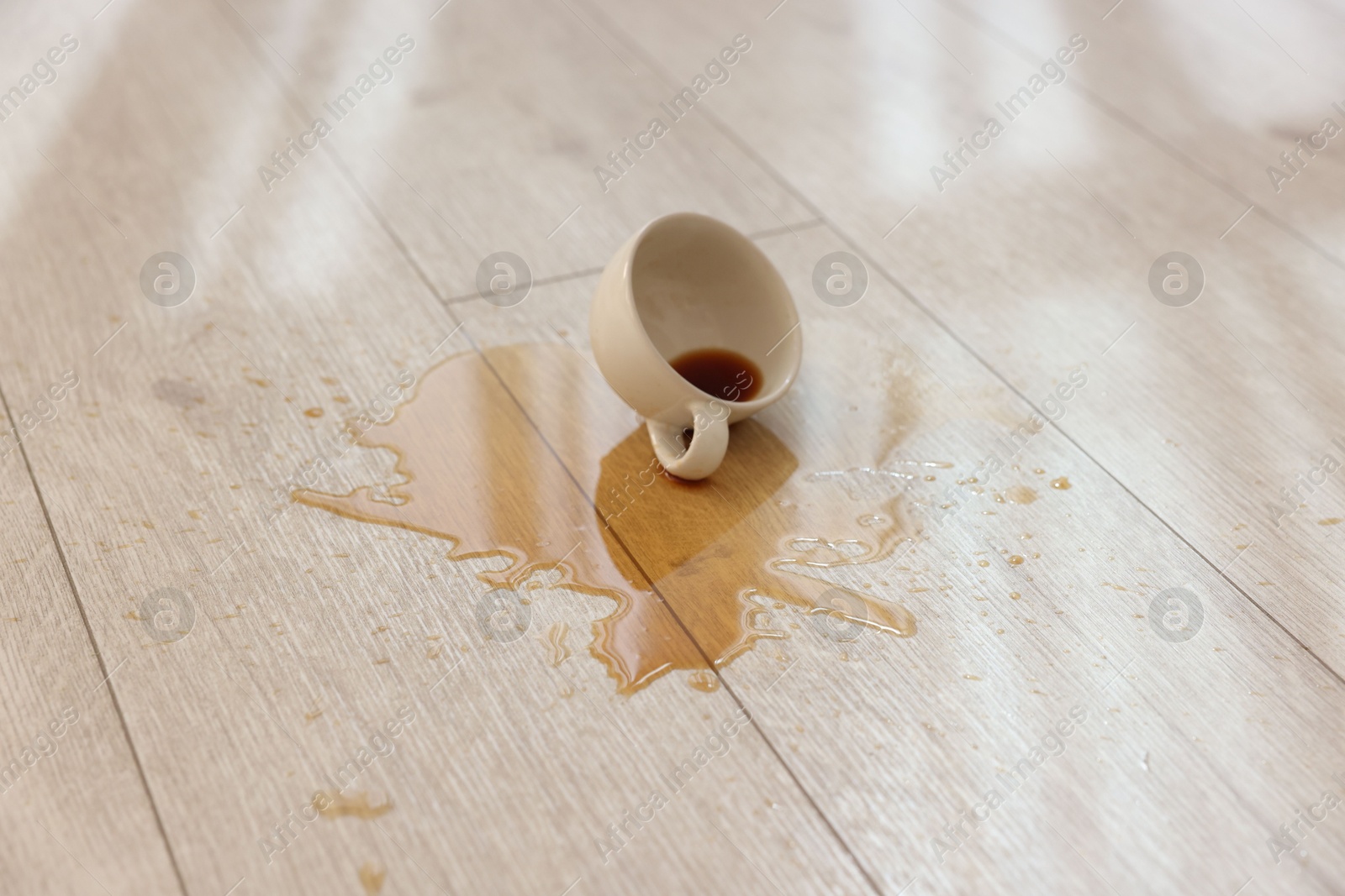 Photo of Cup with spilled drink on wooden floor