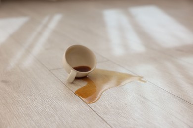 Photo of Cup with spilled drink on wooden floor