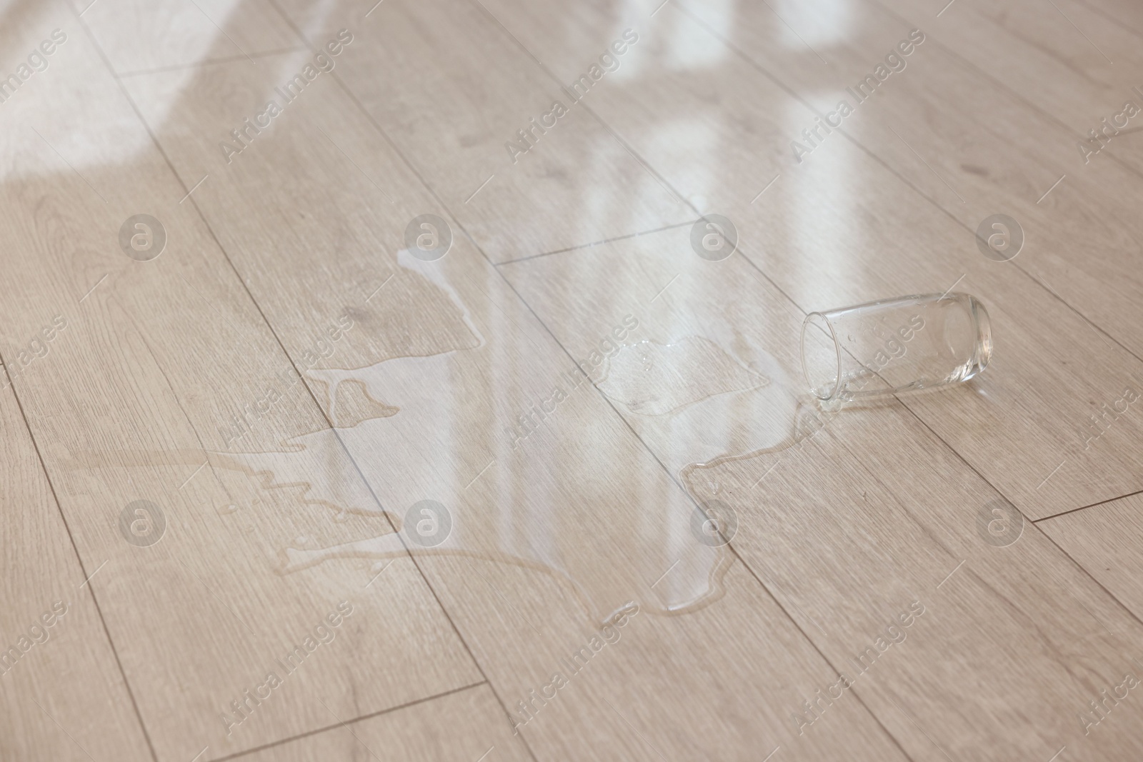 Photo of Glass with spilled drink on wooden floor